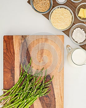 Green asparagus close up on wooden cutting board, and some ingredients close up on kitchen table.