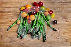 Green asparagus and colorful cherry tomatoes on wooden surface