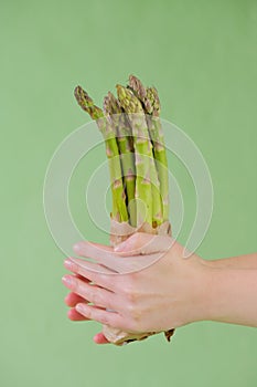 Green asparagus in a craft bag in female hands on a green background.Asparagus season. Spring fresh vegetables. Farmed