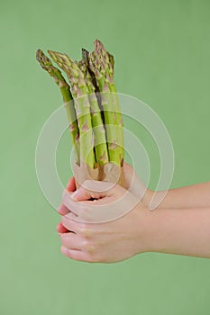 Green asparagus in a craft bag in female hands on a light green background.Asparagus season. Spring vegetables. Farmed