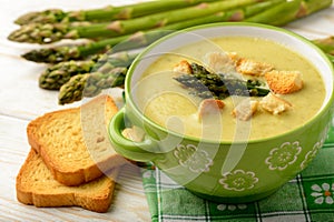 Green asparagus cream soup on wooden background.