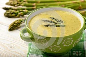 Green asparagus cream soup on wooden background.