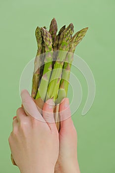 Green asparagus in female hands on a light green background.Asparagus season. Spring fresh vegetables. Farmed Organic
