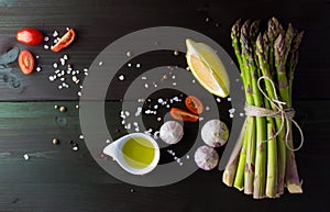 Green asparagus with garlic, salt, lemon, cherry tomato, olive oil and pepper mix on dark background, top view