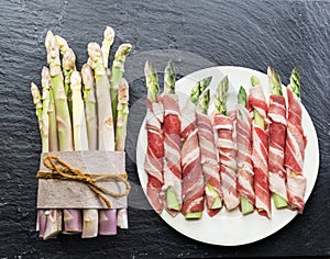 Green asparagus sprouts wrapped in ham on graphite background. Top view