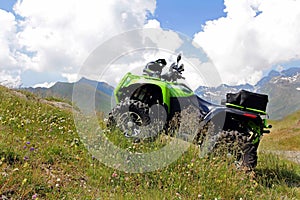 A green ATV stands on a steep mountain path.