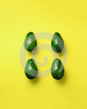 Green avocado pattern on yellow background. Top view. Pop art design, creative summer food concept. Organic avocadoes in