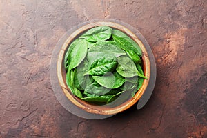 Green baby spinach leaves in wooden bowl on rustic stone table top view. Organic healthy food.