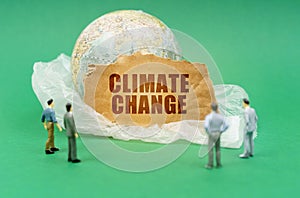 On a green background, blurry figures of people, a plastic bag, a globe and a sign with the inscription - Climate Change