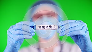 Green background. close-up, doctor`s hands in blue medical gloves holds test tube with inscription sample. doctor