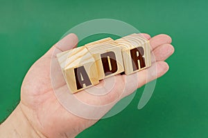 On a green background, in the hands of a person, cubes with the inscription - ADR