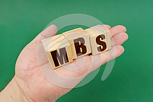 On a green background, in the hands of a person, cubes with the inscription - MBS