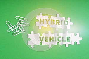 On a green background, paper clips and white puzzles with the inscription - Hybrid Vehicle