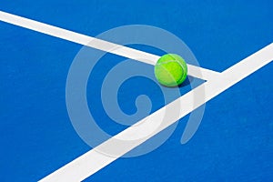 Green ball falling on floor nearly white lines of outdoor blue tennis hard court in public park.