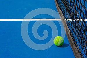 Green ball falling on floor nearly white lines of outdoor blue tennis hard court in public park.