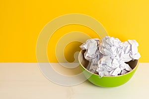 Green bamboo plate and crumpled paper balls on a yellow background and wooden white table. Timing and thinking idea concept. Tima