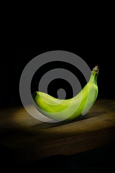 Green banana on wooden board on black background