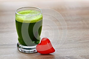 Green barley juice drink in glass and red heart on wood background.