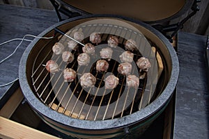 Green BBQ egg grilling meatballs with bacon