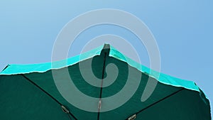 Green beach umbrella. Blue sky in the background. View from below. Relaxing context. Summer holidays by the sea