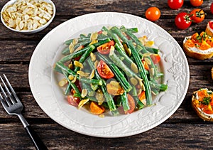Green beans salad with Red, Yellow Tomatoes, bruschettas and flaked almond on white plate