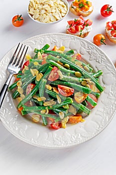 Green beans salad with Red, Yellow Tomatoes, bruschettas and flaked almond on white plate