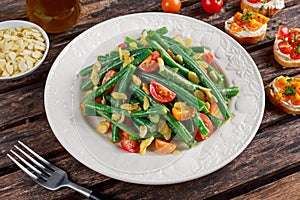 Green beans salad with Red, Yellow Tomatoes, bruschettas and flaked almond on white plate