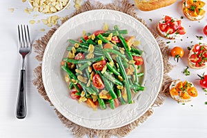 Green beans salad with Red, Yellow Tomatoes, bruschettas and flaked almond on white plate