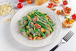 Green beans salad with Red, Yellow Tomatoes, bruschettas and flaked almond on white plate