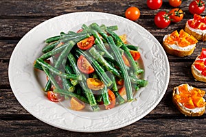 Green beans salad with Red, Yellow Tomatoes, bruschettas on white plate