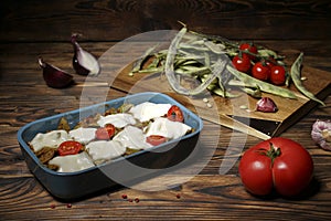 green beans and tomatoes with cheese in a baking dish on a wooden rustic table.