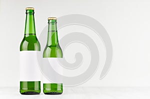 Green beer bottles longneck 500ml and 330ml with blank white label on white wooden board, mock up.