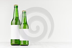 Green beer bottles longneck 500ml and 330ml with blank white label on white wooden board, mock up.