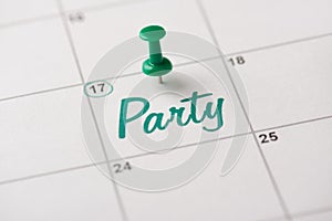 Green beer party is almost here concept. Cropped close up view photo of thumb tack attached to white calendar with word party