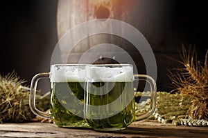 Green beers on a wooden table, in the back of the original oak barrel and wheat cob. There`s an oak barrel in the background