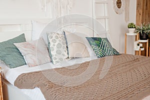 Green, beige pillow on bed in bedroom with pastel colored bedsheets on bed. stylish white apartment design in lagom