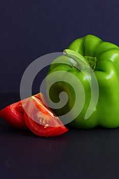 Green bell pepper, Capsicum annum, and red tomato pieces against a dark blue background with copy space.