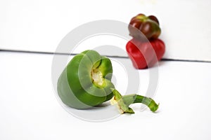 A green bell pepper with its head cut off next to two red bell peppers fade on a white background