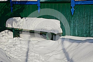 Green bench against a wall in white snow