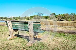 Green bench align to the left on a very peaceful place in a park with green vegetation and the lake