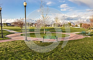 Green benches around a circular pathway on a park with trees and lamp posts