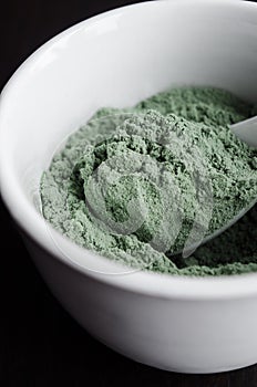 Green bentonite clay powder in the bowl. Diy facial mask and body wrap recipe. Dark background, clay texture close up photo