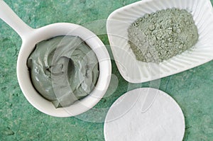 Green bentonite clay in a small white bowl. Clay texture close up. Diy mask and body wrap recipe. Natural beauty treatment and spa