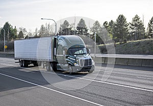 Green big rig semi truck transporting frozen cargo in refrigerated semi trailer running on the wide highway road