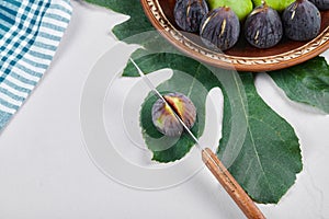 Green and black figs on a ceramic plate with a knife and a leaf