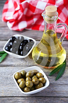 Green and black olives in bowl on grey wooden background.