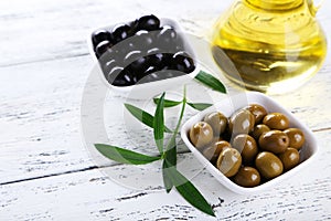 Green and black olives in bowl on white wooden background.