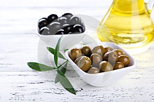 Green and black olives in bowl on a white wooden background