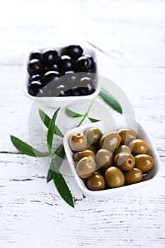 Green and black olives in bowl on the white wooden background