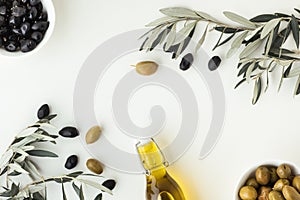 Green and black olives in white bowls next to a bottle with olive oil and leaves on a white background. .Bottle of cold pressed